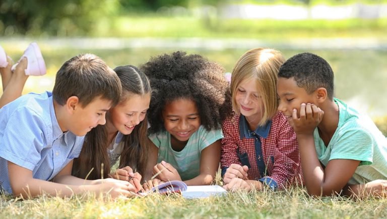 Young Kids Reading Book on Grass Outside