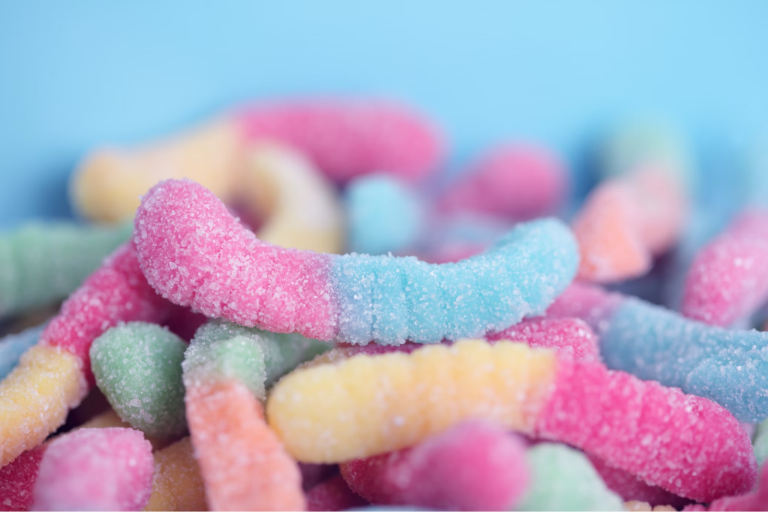 A close up shot of a pile of colorful sour gummy worms against a light blue bakground.